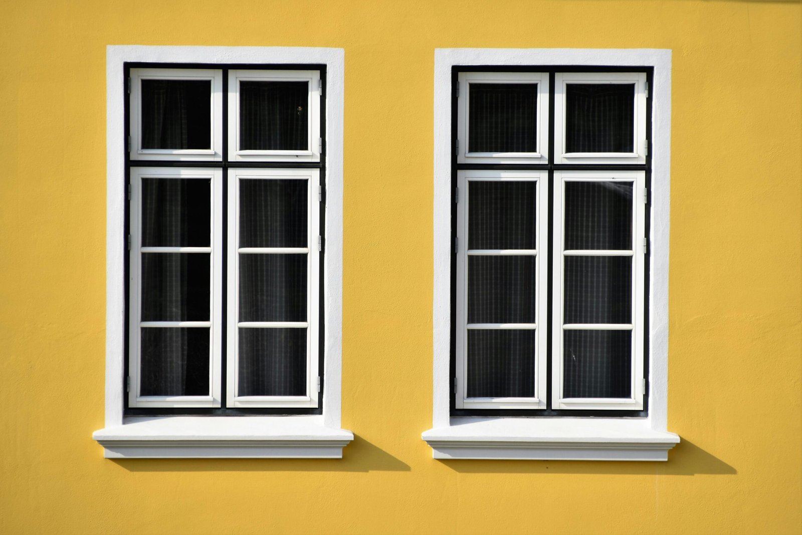 Two white-framed windows on a vibrant yellow building facade in Büsum, Germany.