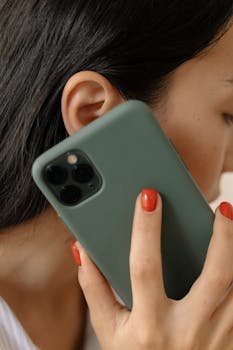 A woman with red nails holds a smartphone to her ear, close-up view.