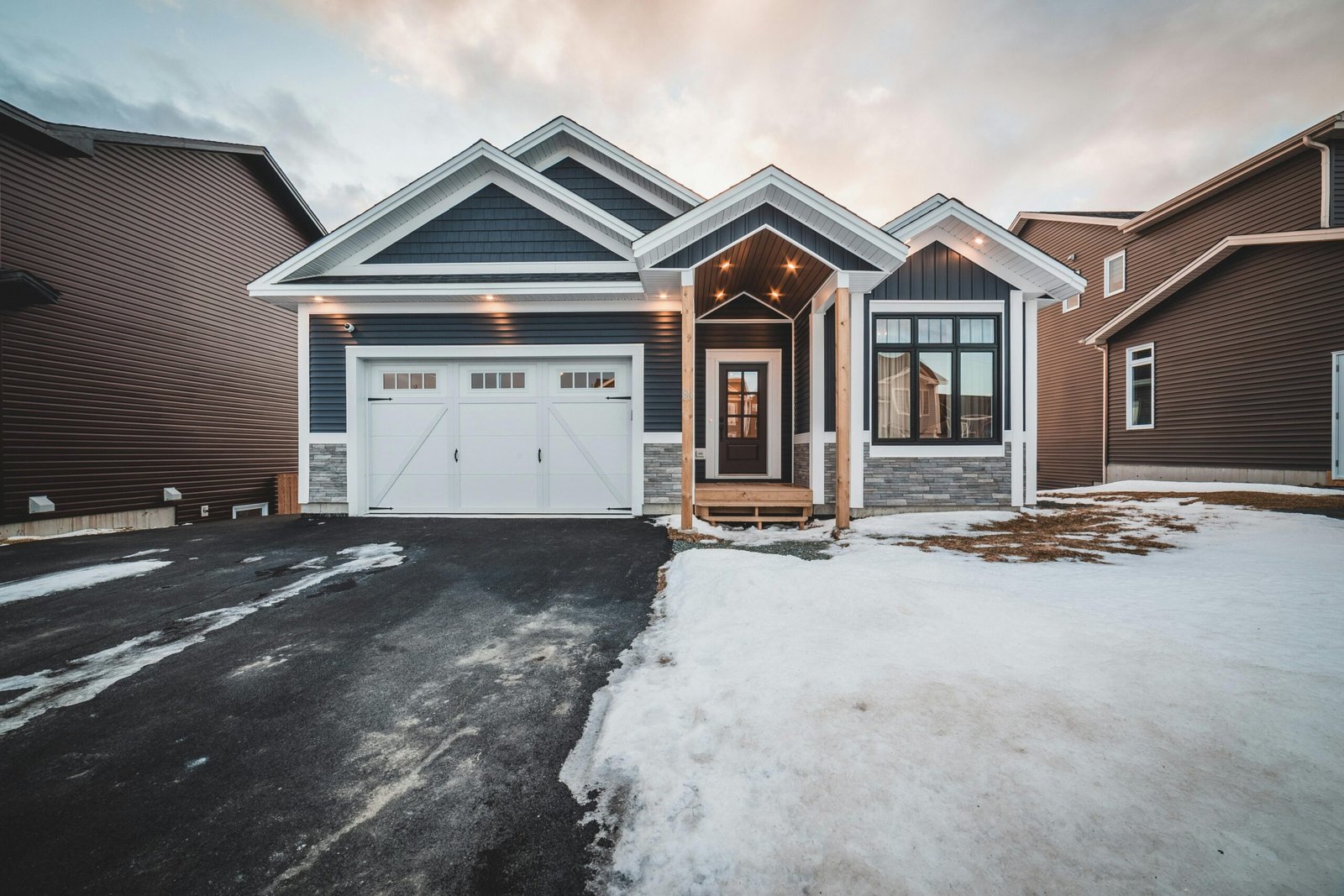 Exterior of modern blue cottage house surrounded by residential houses and snow in daylight